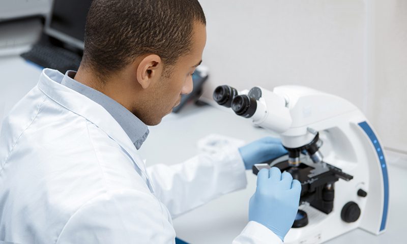 A man in lab coat looking through microscope.